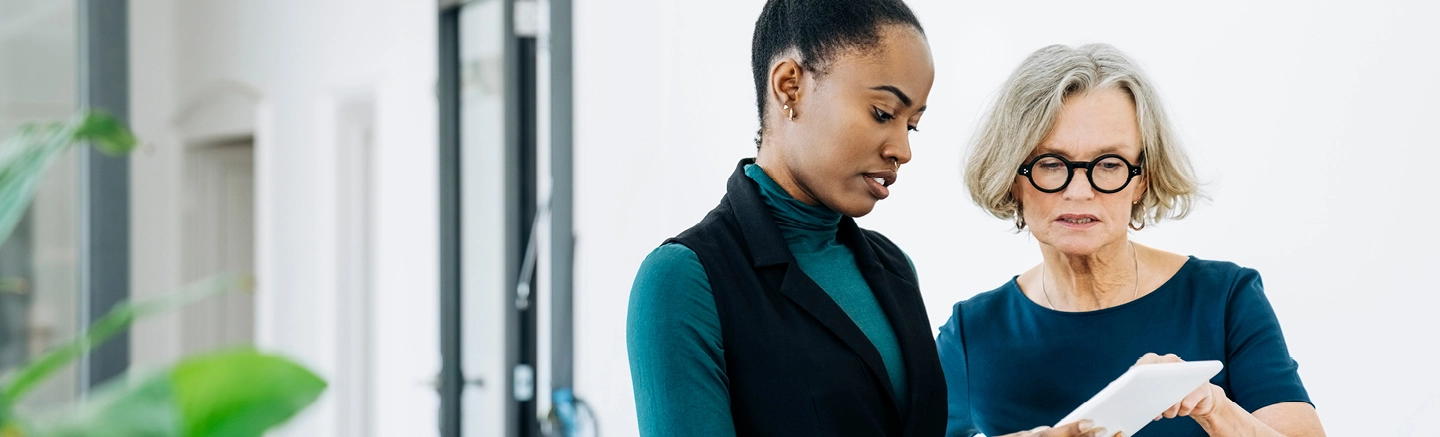 Black woman and older woman professionally dressed looking at iPad.