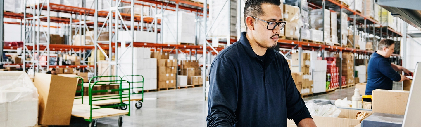 Man with glasses looking at computer on retail warehouse floor