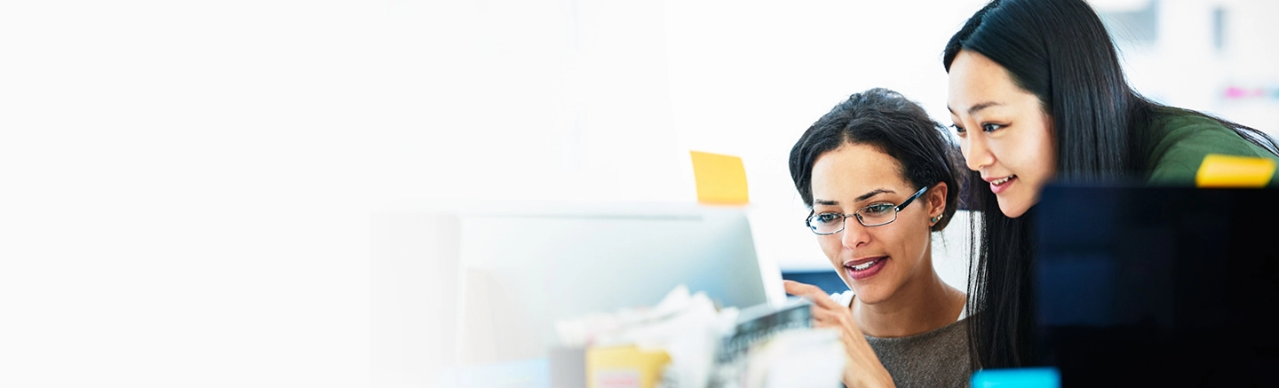 Two diverse women looking at an Apple desktop in office