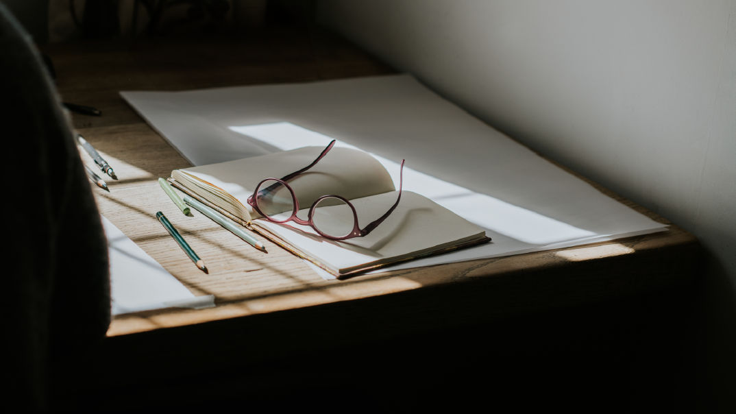 Un livre ouvert posé sur une table, avec des lunettes roses et des crayons de couleur.