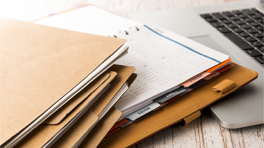 Plusieurs chemises en papier kraft et un agenda jaune posés sur un ordinateur portable gris.