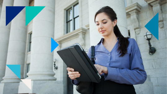 A woman wearing a blue shirt and a ponytail looks into a tablet with a white building in the background.