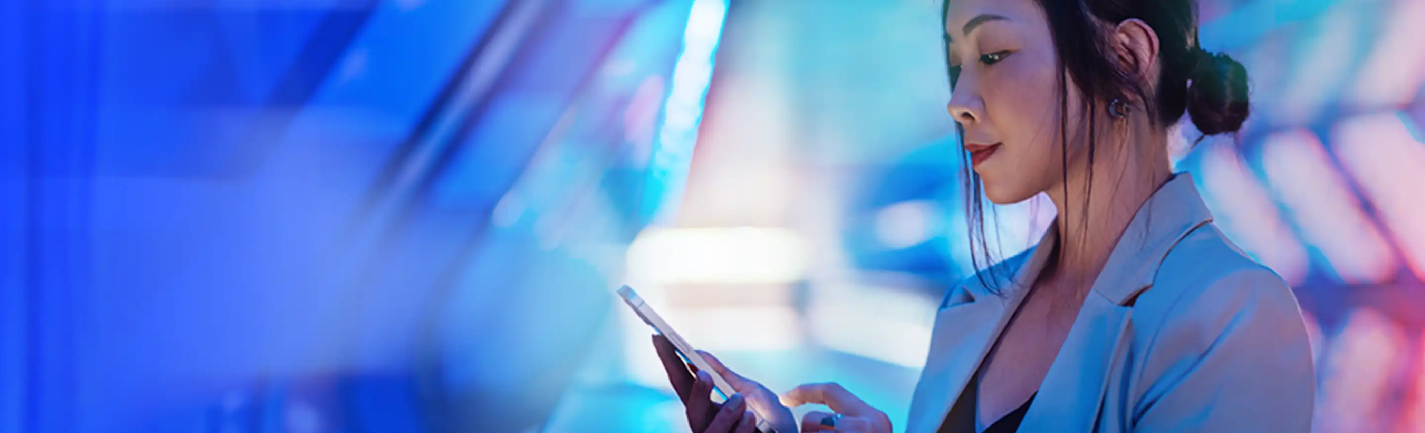 A woman looks into her cell phone on a blue and pink background.
