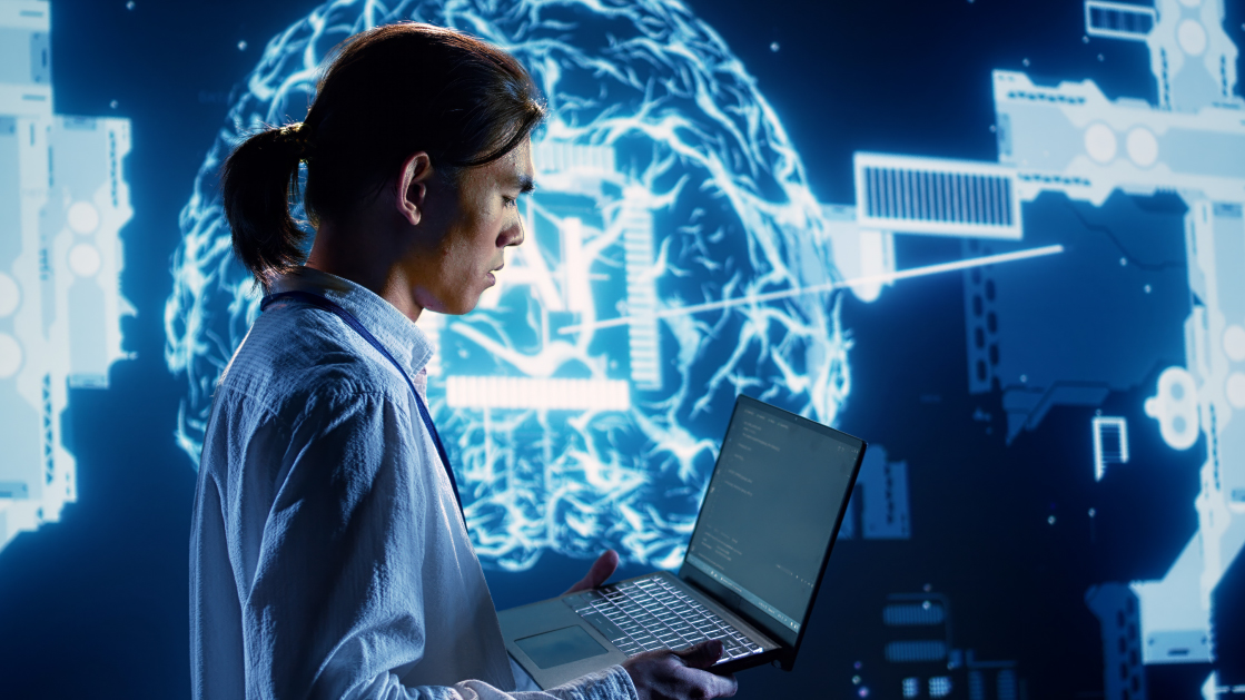 Un homme en chemise bleue et queue de cheval porte et regarde un ordinateur portable. Derrière lui, une projection bleue d'un cerveau avec les mots « AI ».