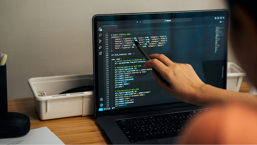A picture of a hand, likely a Java Developer, using a black pen to point to something on an HTML code on a laptop.